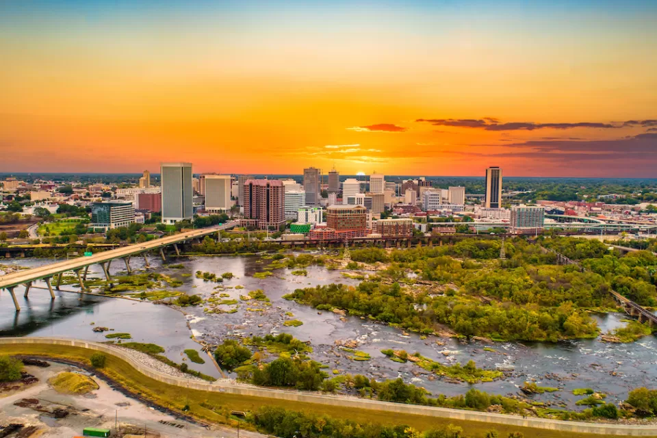 Aerial view of Richmond, Virginia skyline with river in foreground against sunset sky.